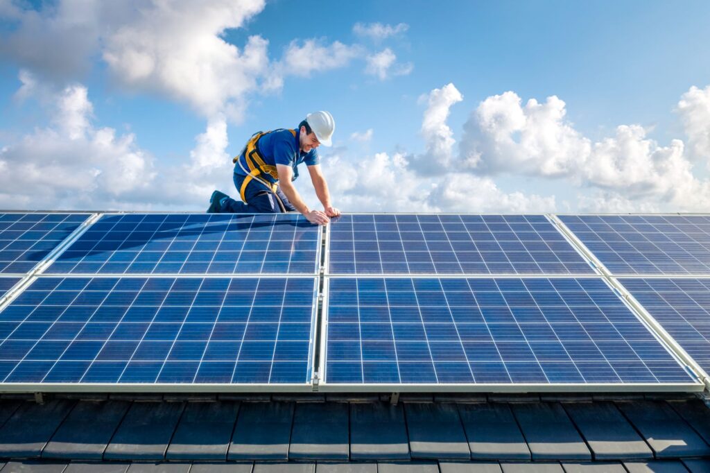 Solar installer kneeling on a residential roof installing photovoltaic panels